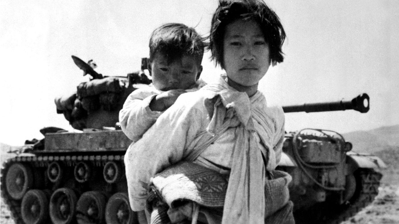 Girl with baby on her back standing in front of a tank