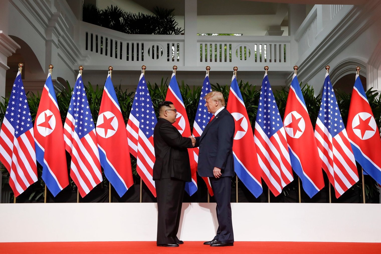 Trump and Kim in Singapore shaking hands in front of flags